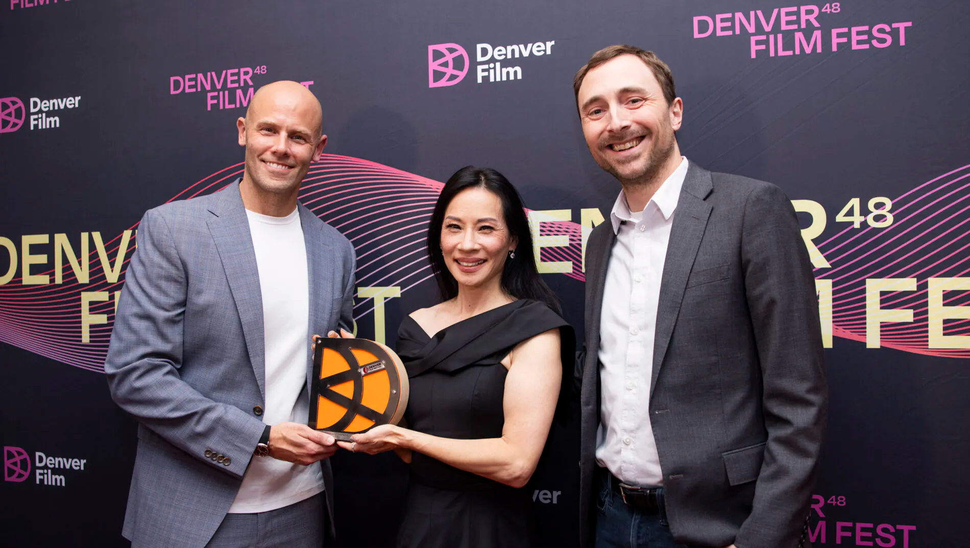 [gpt-4o]: Three people smiling at Denver Film Fest backdrop, one holding an award