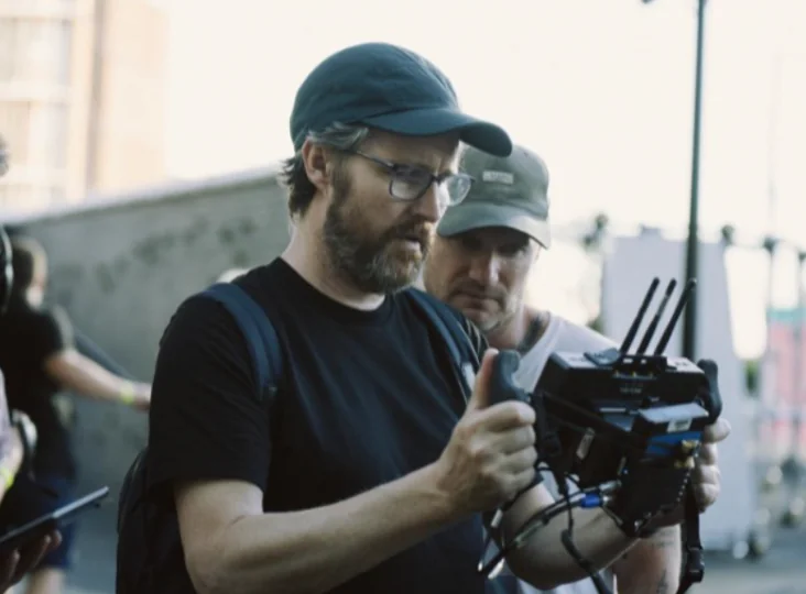 Filmmaker adjusting camera rig with two people observing beside him [Model: gpt-4o]