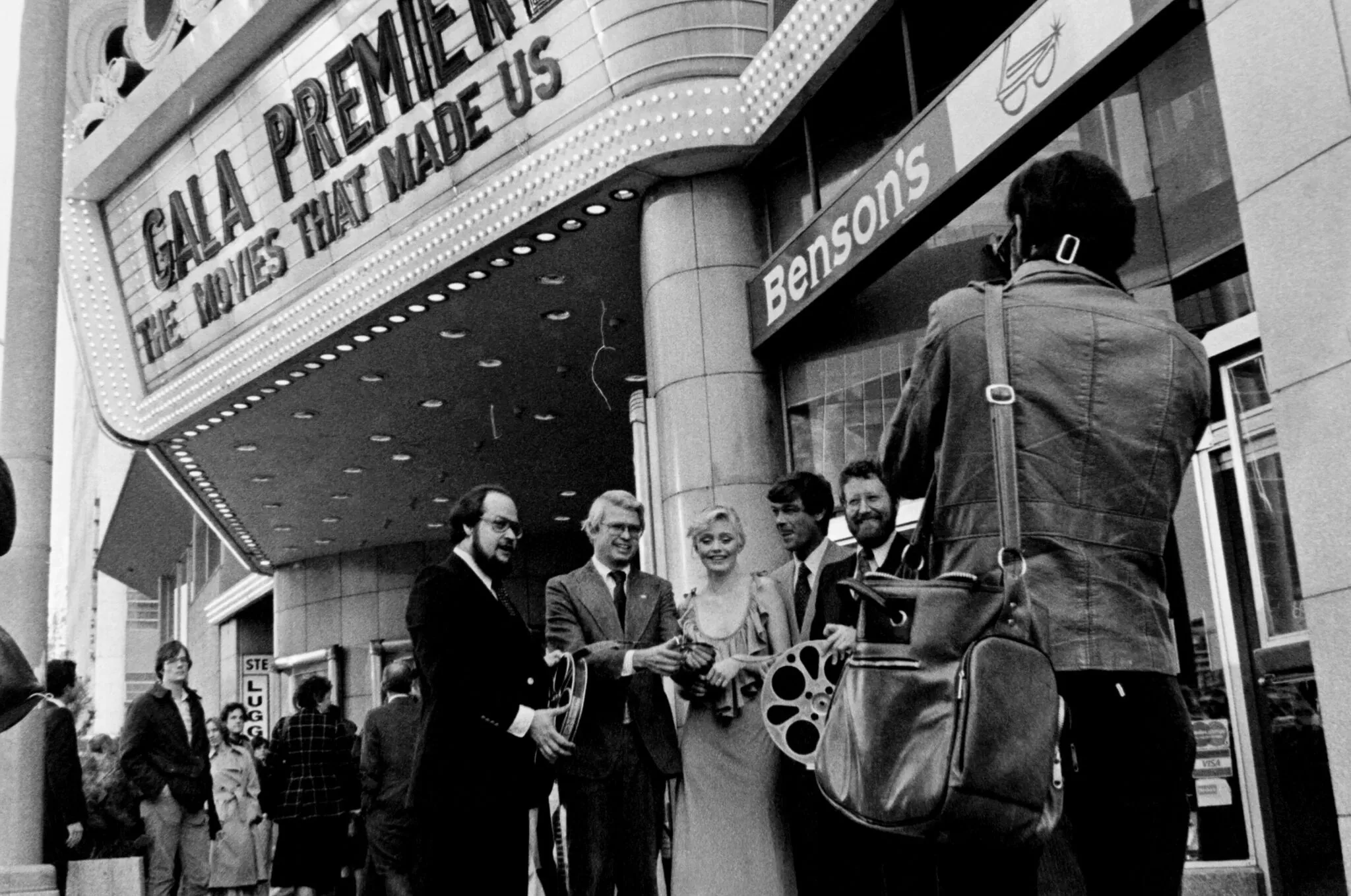 [gpt-4o]: Group of people smiling at theater premiere; marquee reads "Gala Premiere: The Movies That Made Us"