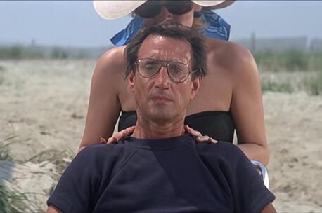 Man sitting on beach with woman standing behind, hands on shoulders